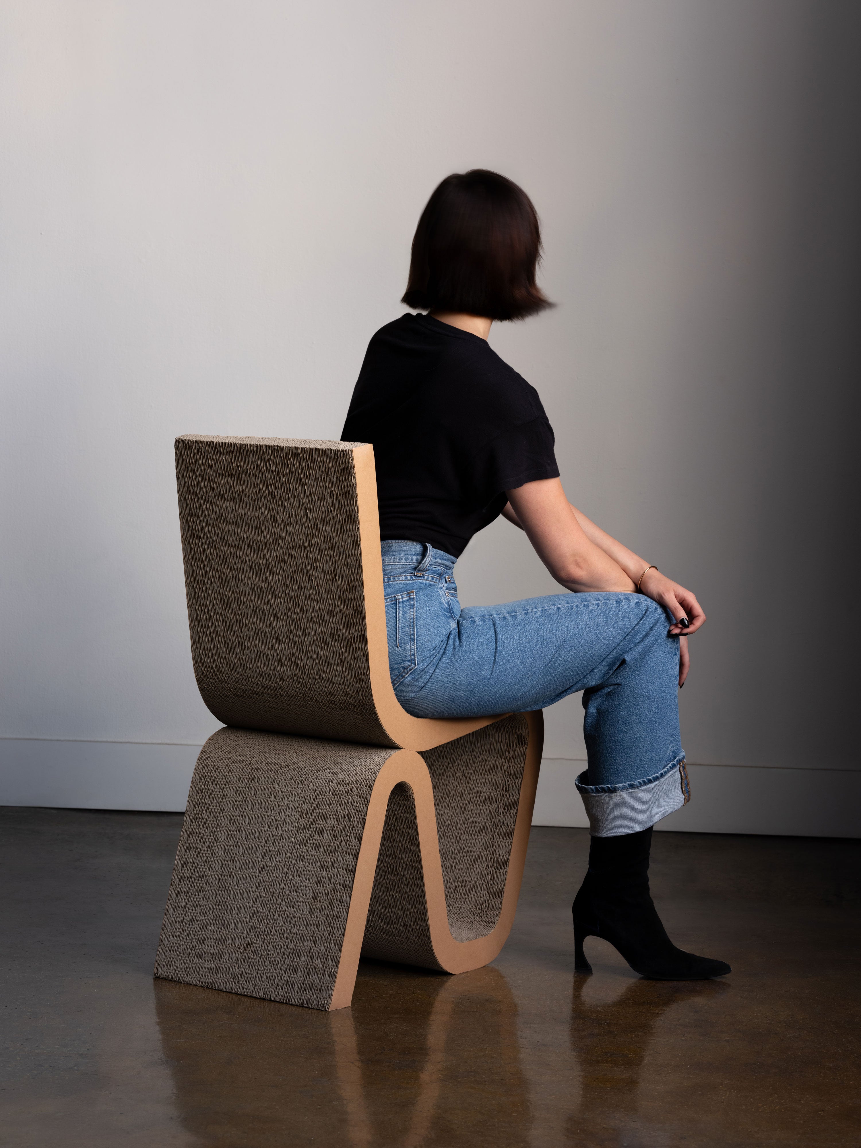Person sitting on sculptural cardboard Rumi Chair, showing durability and design of modern cat scratcher furniture